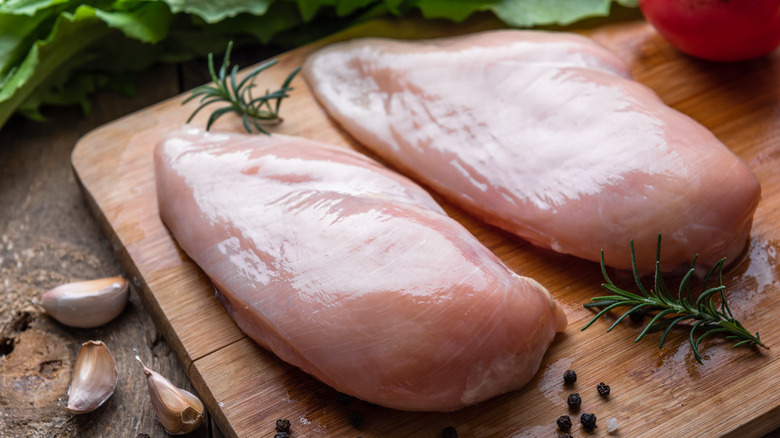 Two raw chicken breasts on a cutting board with herbs.