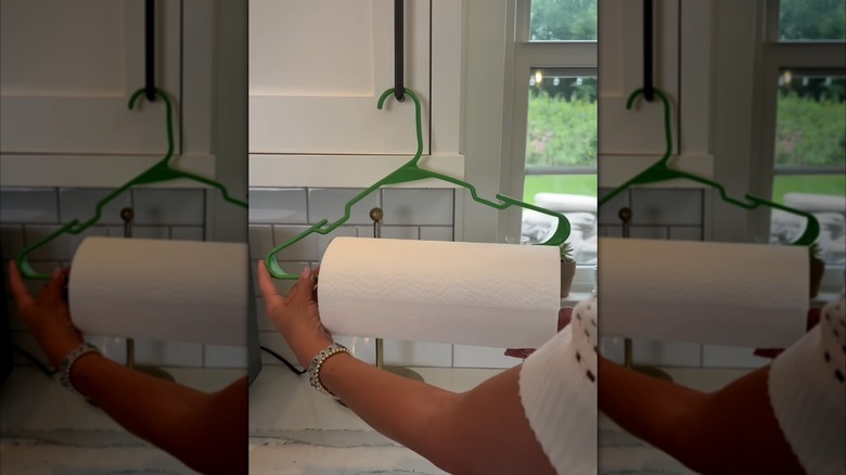 Person hanging a paper towel roll with a green plastic clothes hanger