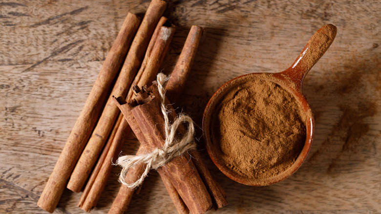 A bowl of ground cinnamon sitting next to several sticks of cinnamon