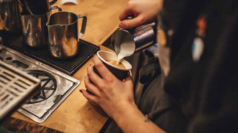 A female barista pouring milk to make a cup of cappuccino coffee in a coffee shop