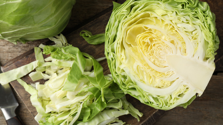 Fresh cut cabbages and knife on wooden table, flat lay