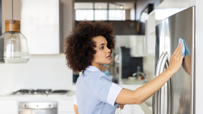 Woman cleaning the fridge with a cloth and solution