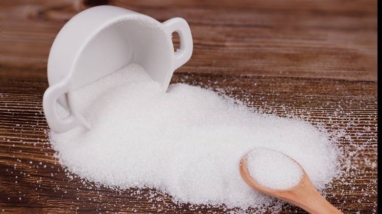 Granulated sugar spilled out onto a cutting board.