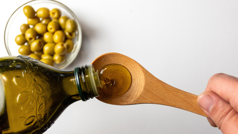 Olive oil being poured from tinted glass bottle into wooden spoon