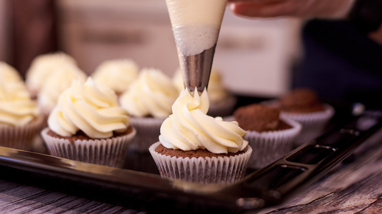 Baker piping cream cheese frosting on to cupcakes