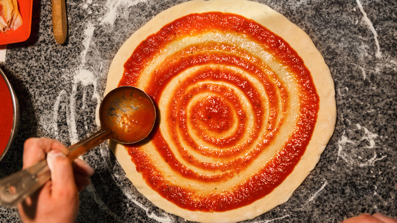 Adding sauce to pizza