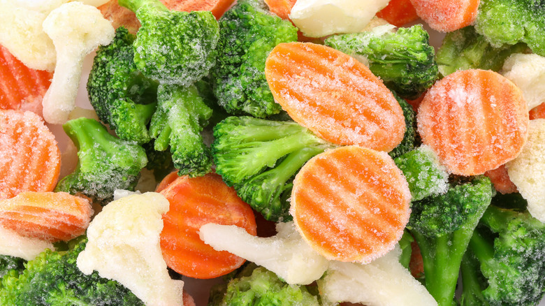 A close-up image of frozen broccoli, cauliflower, and carrots with frost forming around them.