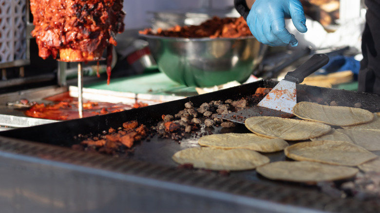 Street vendor heating tortillas and chopped al pastor meat on a grill