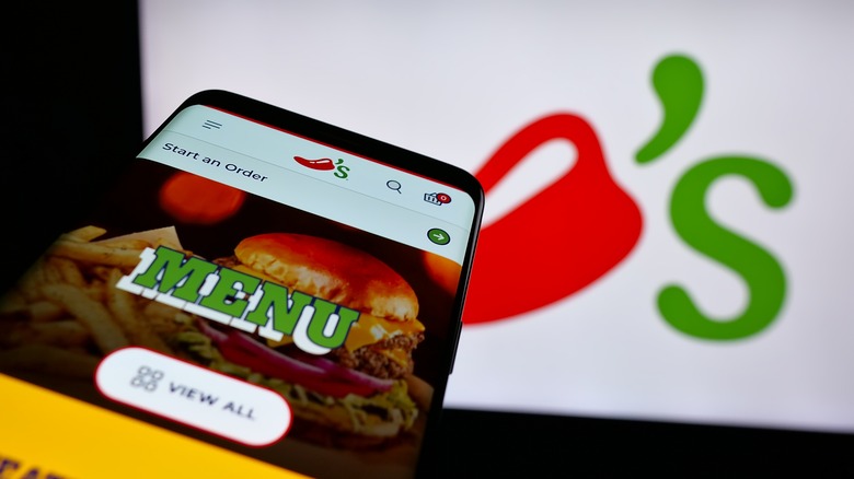 Chili's menu on a phone held in front of a Chili's signboard