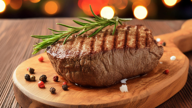 A well-grilled steak topped with a rosemary sprig and garnished with cranberries on a wooden palette