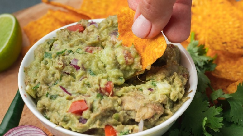 A hand dipping a chip into fresh guacamole made with avocados.