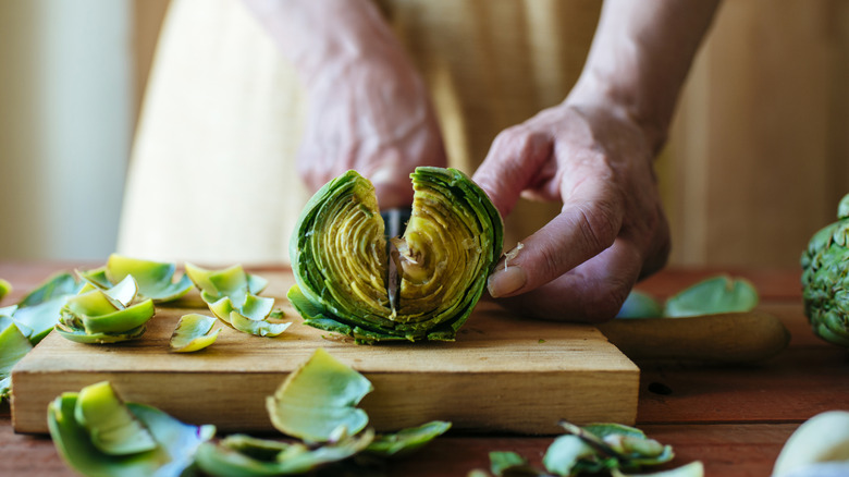 hands chopping artichoke in half on cutting board