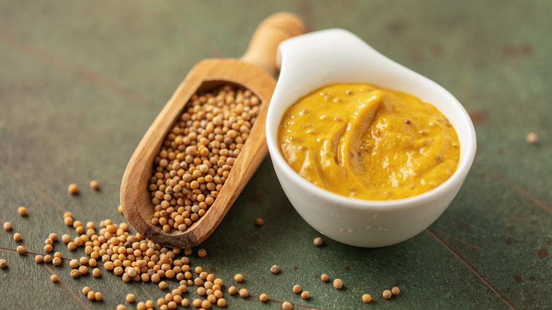 yellow mustard in a bowl next to whole mustard seed