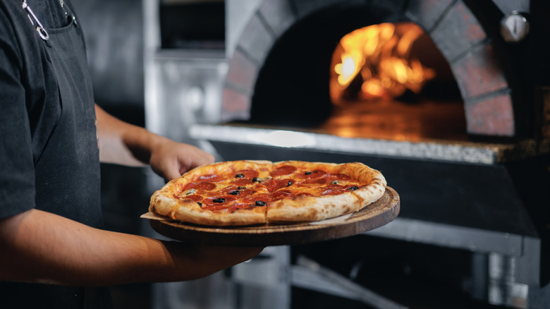 A traditional pizza maker holding a freshly baked pizza.