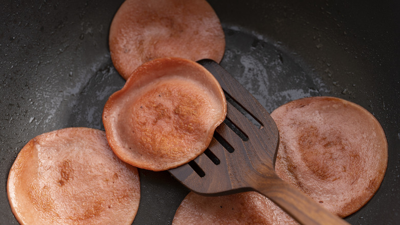 Flipping slices of fried bologna with a wooden spatula in a frying pan