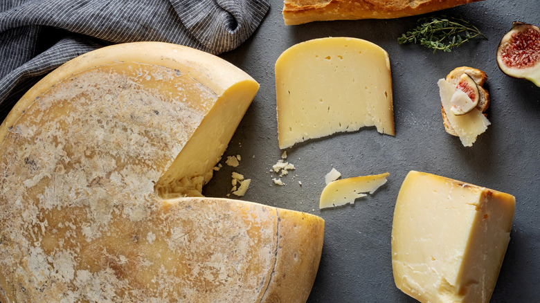 A cheese wheel with a wedge cut out on a gray surface.