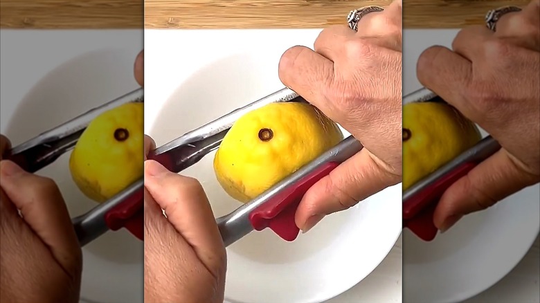 Hands squeezing half of a lemon with kitchen tongs over a white bowl