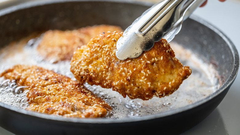 Crispy fried chicken cutlets being removed from a pan.