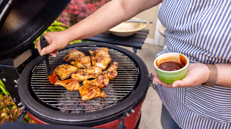 Person basting chicken thighs and legs with barbecue sauce