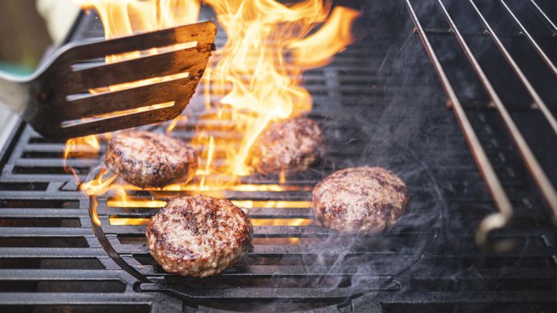 Burgers on grill with high flames rising through grill grates