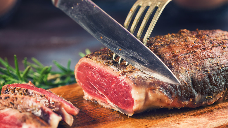 Fork holding medium rare brisket roast while knife slices off pieces