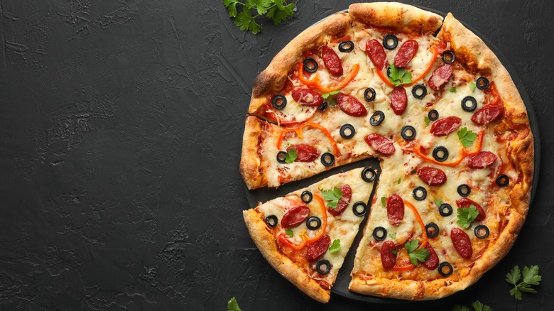 A freshly made pizza on a plate with olives and peppers