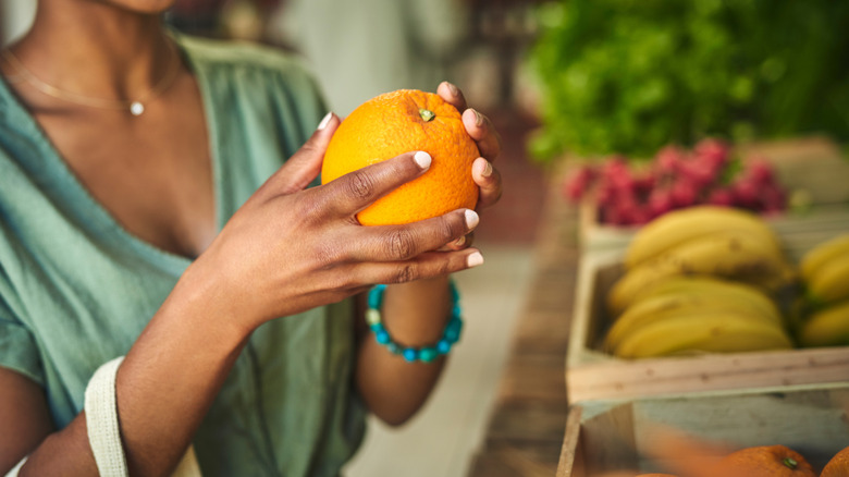 closeup of osmeones hand holding an orange in the produce aisle