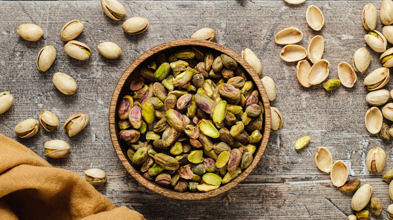 Bowl of shelled pistachio nuts with shells scattered around the bowl