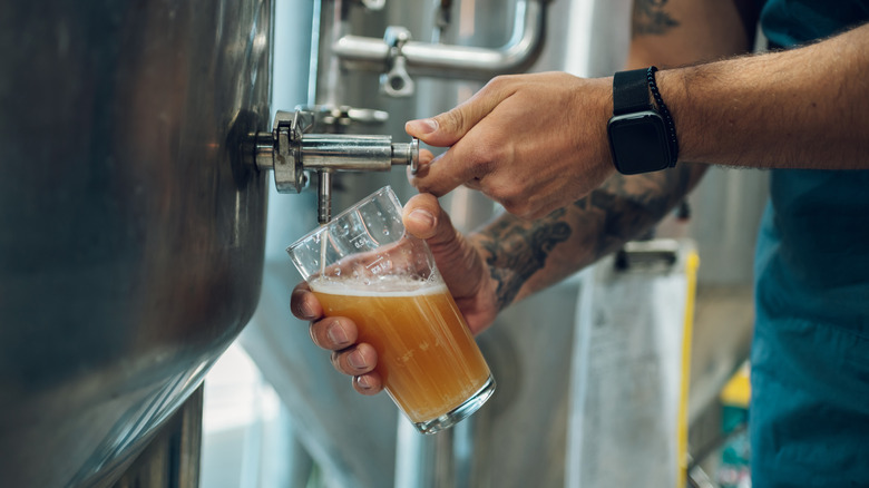A person pouring beer into a glass from a brewery's fermentation vessel