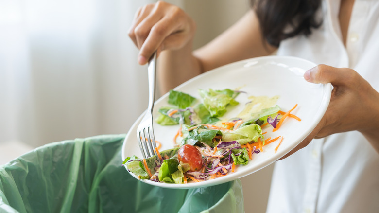 Woman pouring uneaten food into a bin