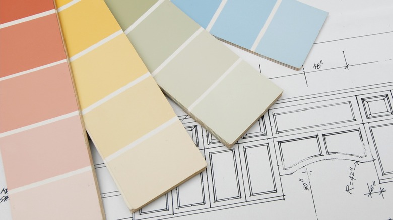 Four paint sample cards sit next to plans for a kitchen