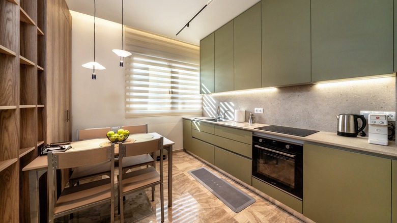 Kitchen pairs olive green cabinets with cream walls and mocha shelving