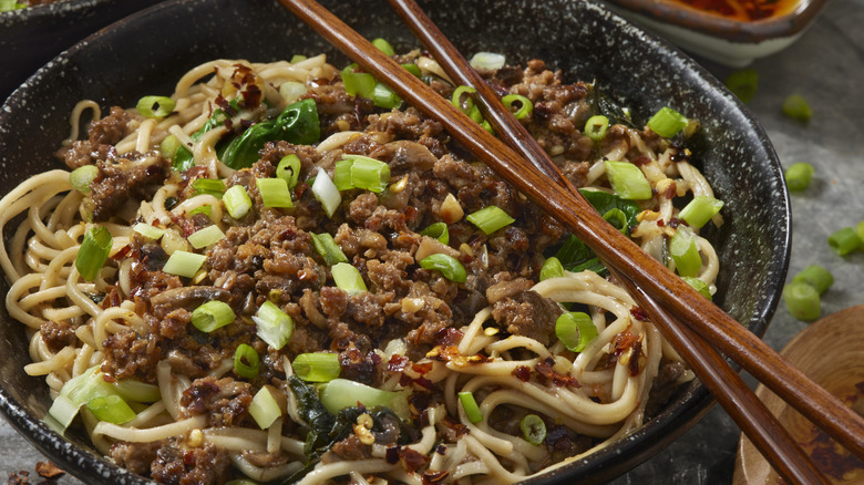 A close-up of dan dan noodles garnished with ground meat and spring onions