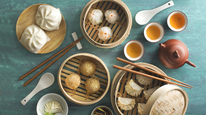 A flatlay of Chinese favorites like sesame balls, dumplings, and steamed buns, served with three cups of tea
