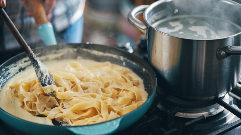 preparing fettucine pasta in Alfredo sauce on a stove