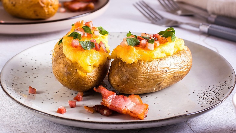 Two twice-baked potatoes with melted cheese, crumbled bacon, and chopped greens on a white-speckled plate