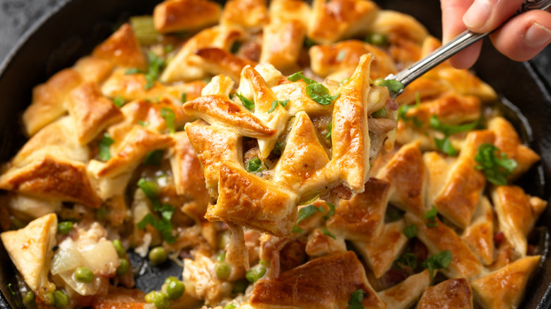 Person scooping chicken pot pie out of a cast iron pan