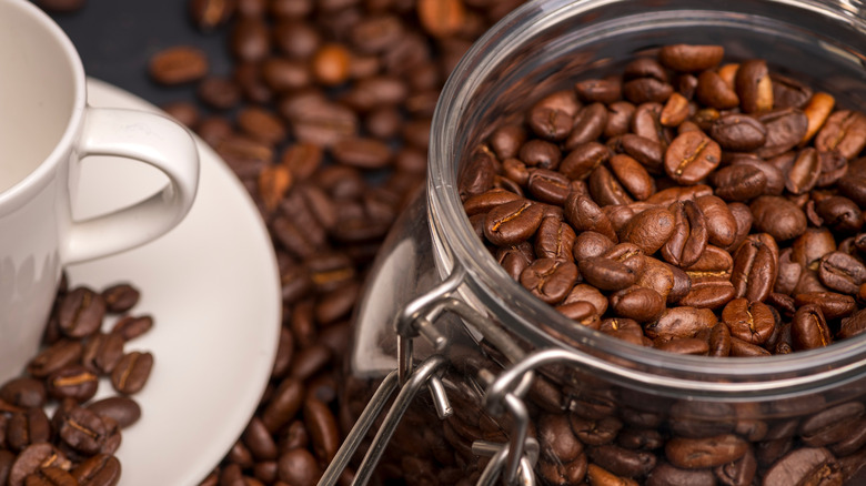 mason jar filled with coffee beans on counter next to coffee cup.