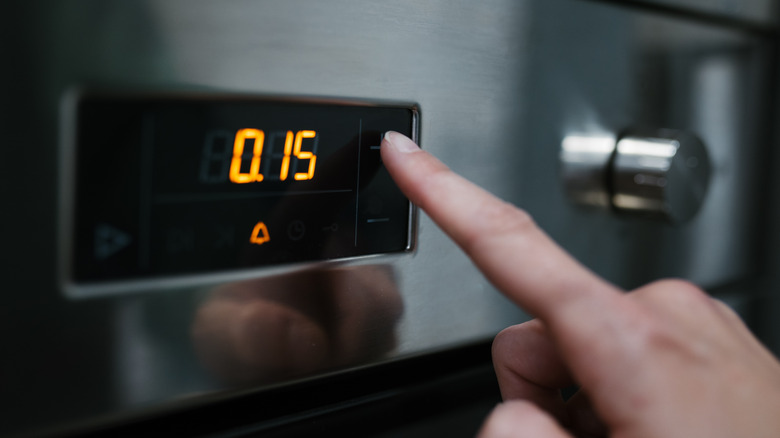An individual pressing a button on an oven's digital control panel.