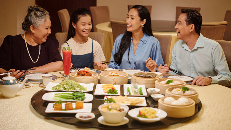 A smiling family sits at a table in a restaurant with numerous Chinese food dishes on a lazy Susan