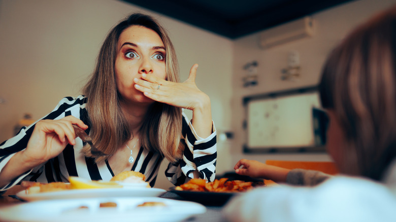 A woman covering her mouth in embarrassment while she eats