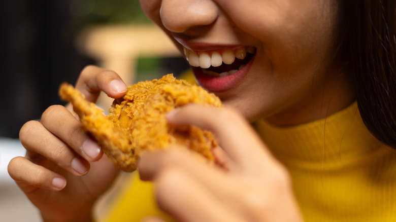 A smiling woman about to take a satisfying bite of a crunchy fried chicken