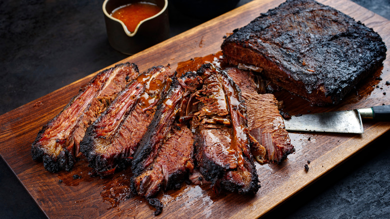 Sliced smoked brisket on a wood cutting board against a dark background