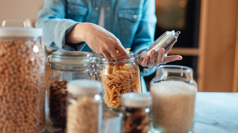 Person putting dry goods into various clear jars