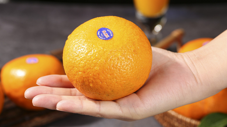 Fresh orange with blue produce sticker held in hand