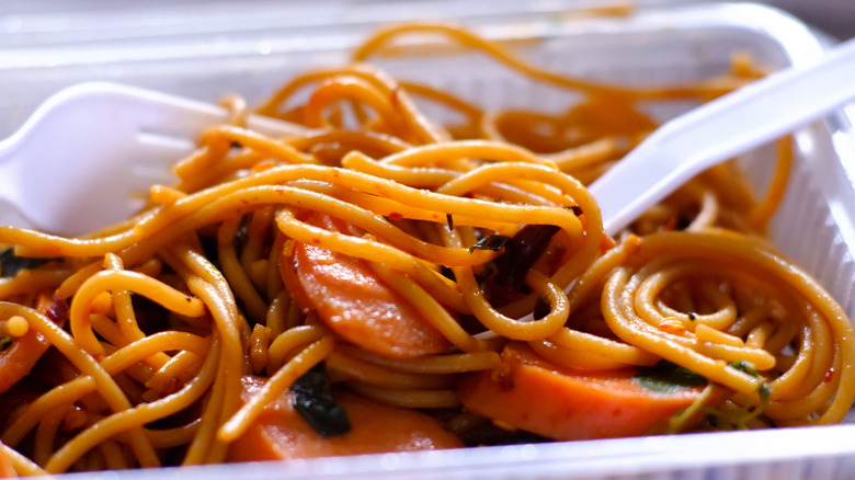 Oily, saucy noodles in a plastic container with plastic forks