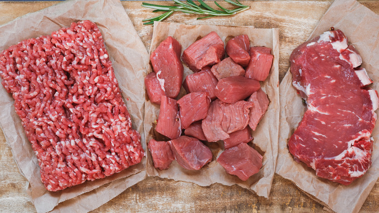 Various cuts of raw meat on parchment paper sitting on a wooden cutting board.
