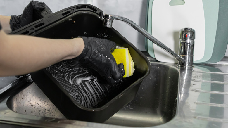 Person wearing black gloves washing an air fryer basket