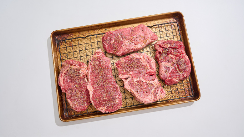 Salted raw steaks on a wire rack-fitted sheet tray
