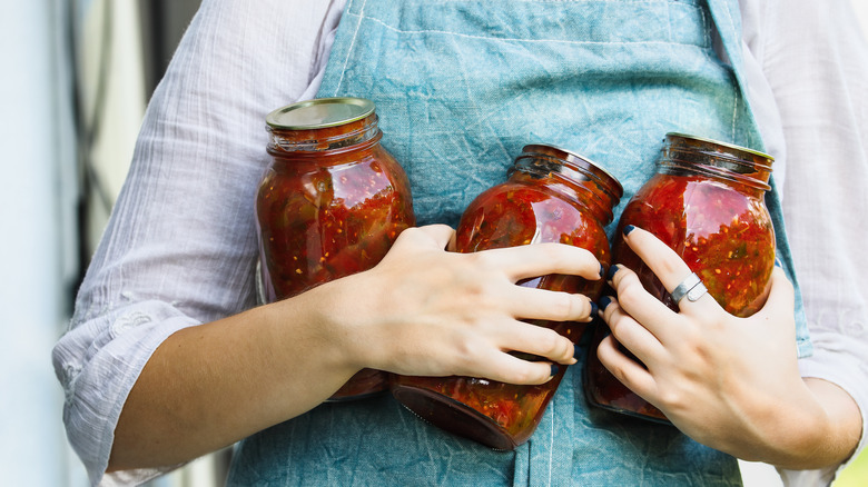 A women in an apron holding mason jars filled with homemade jam